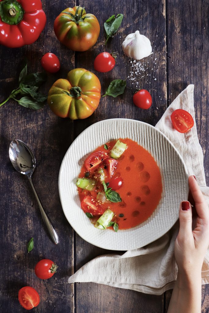 gazpacho di pomodori cetrioli e peperoni visto dall'alto, in piatto bianco appoggiato su tavolo in legno scuro grezzo