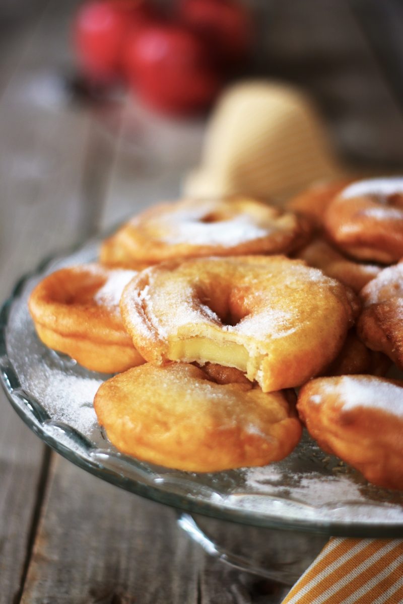 Primo piano di una frittella di mele con un morso, mostrando il cuore di mela avvolto in una pastella croccante, decorata con zucchero a velo.