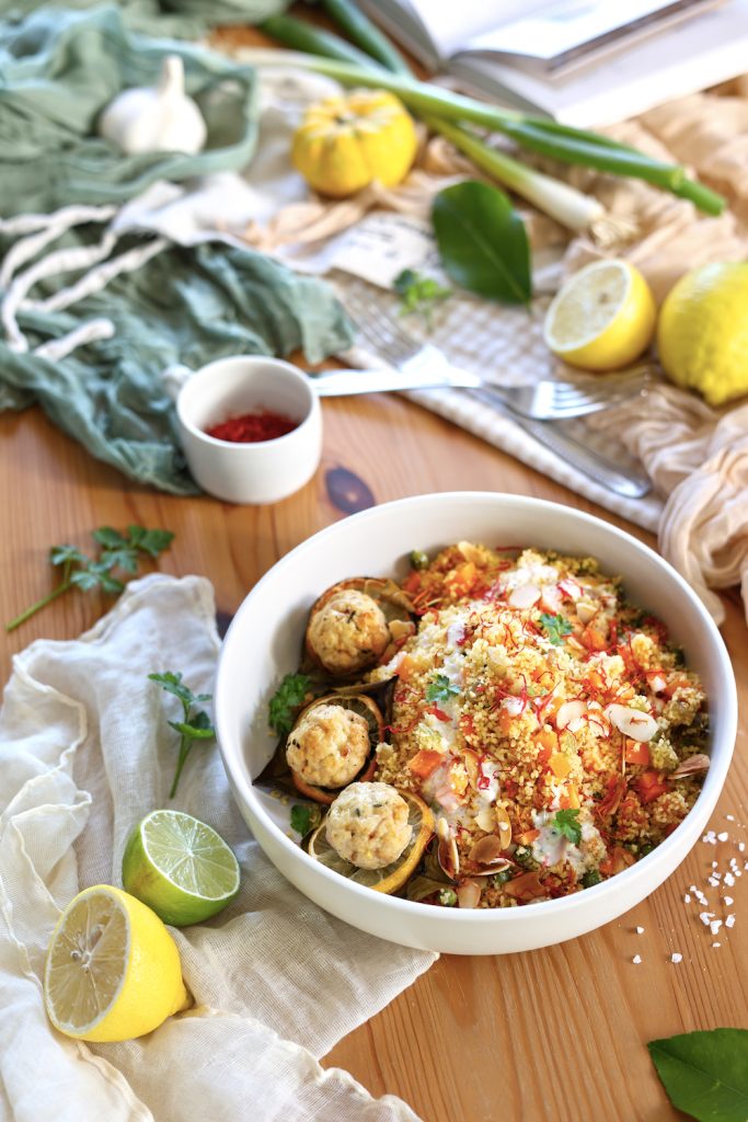 Cous cous alle verdure d'inverno con polpette di tacchino al limone servito su una bowl bianca in una tavola con limoni