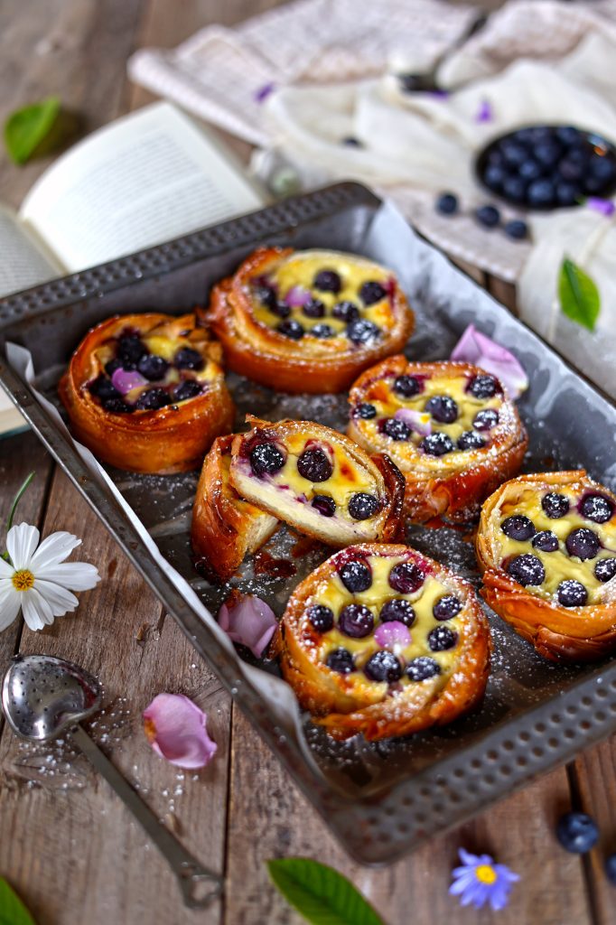 Mini cheesecake tart ai mirtilli e limone in una teglia da forno su un tavola rustica, decorata con dei fiori colorati