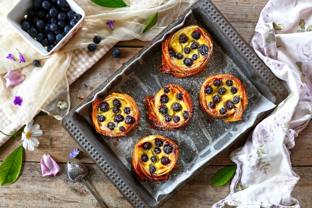Visione dall'alto della teglia da forno con cinque mini cheesecake tart ai mirtilli e limone, in una tavola rustica